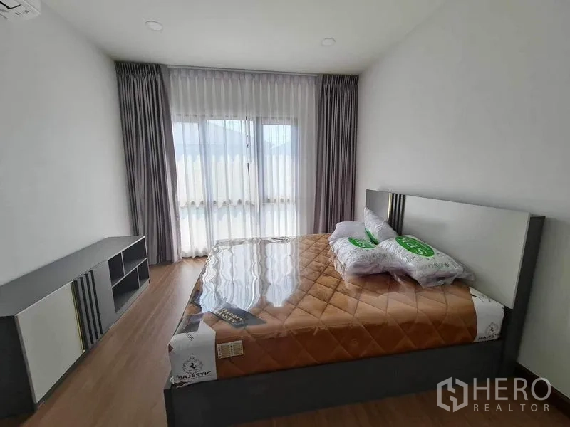Detached House for rent or sale in Bang Phli, Samut Prakan - Sunlit bedroom with double bed, floor-to-ceiling curtains and built-in console.