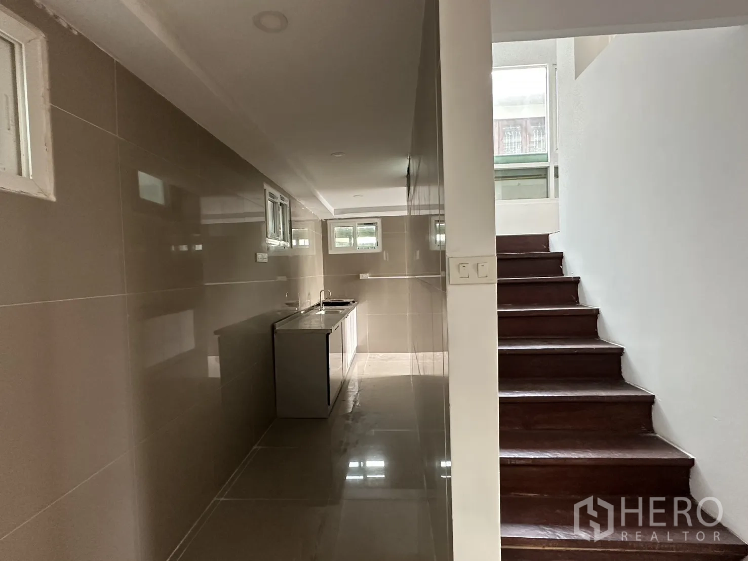 Home Office for rent in Watthana, Bangkok - Long galley kitchen with tiled walls, countertop sink and adjacent staircase.