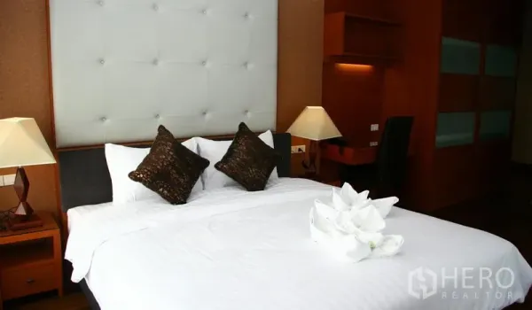 Apartment for rent in Khlong Toei, Bangkok - Cozy bedroom with white padded headboard, bedside lamps and a king-size bed