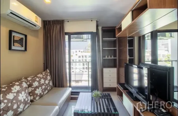 Apartment for rent in Bang Rak, Bangkok - Bright living room with sofa, TV cabinet, built‑in shelving and a balcony city view in a Silom apartment.