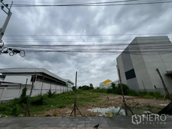 Land for sale - Streetfront view of empty land between warehouses with overhead power lines and a tiled sidewalk.