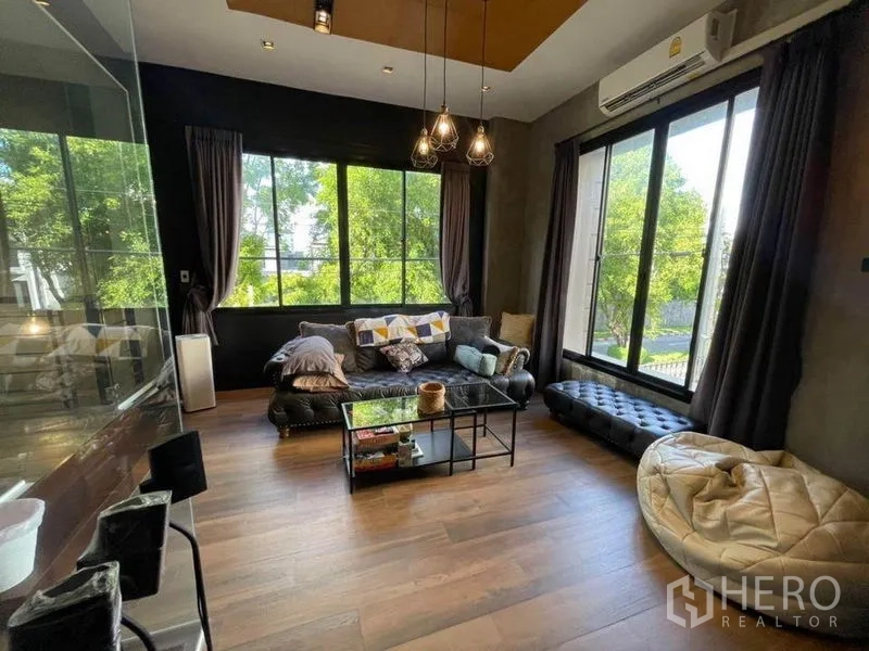 ทาวน์เฮาส์ ขายในBang Phli, Samut Prakan - ห้องรับแขกโปร่งสว่างด้วยหน้าต่างบานใหญ่ มองเห็นต้นไม้ภายนอก พื้นไม้และโซฟาหนัง.