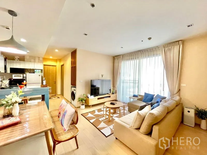 คอนโด ให้เช่าหรือขายในWatthana, Bangkok - ห้องนั่งเล่นคอนโดโทนสว่าง โซฟาตัวแอล ทีวี ประตูกระจกเปิดสู่ระเบียง และเคาน์เตอร์ครัว