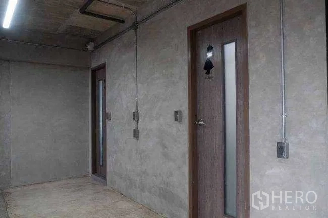 Office Space for rent or sale in Lak Si, Bangkok - Concrete corridor with two wooden restroom doors and exposed conduits.