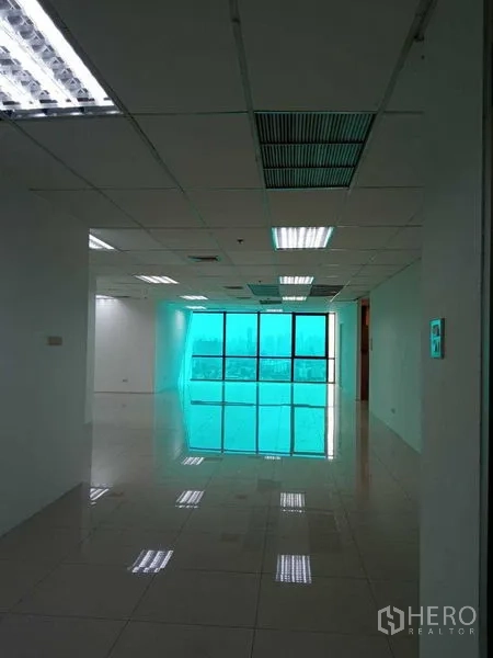 Office Space for rent in Huai Khwang, Bangkok - Open-plan office with glossy tile floors, suspended ceiling lighting, and large tinted floor-to-ceiling windows with Bangkok city views.