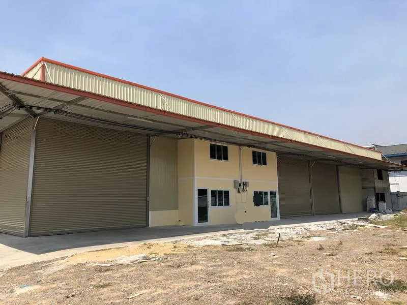 Factory for rent in Khlong Luang, Pathum Thani - Wide view of the factory facade showing multiple roller shutter doors and a concrete yard.