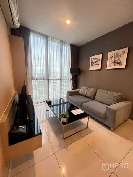 คอนโด ให้เช่า - ห้องนั่งเล่นอบอุ่น โซฟาสีเทา ชั้นวางทีวี และหน้าต่างเต็มผนังมองเห็นวิวสกายไลน์กรุงเทพฯ