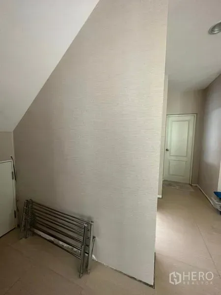 独立式住宅 出售在Prawet, Bangkok - 楼梯下方过道与白色门，采光明亮的独栋别墅内部。