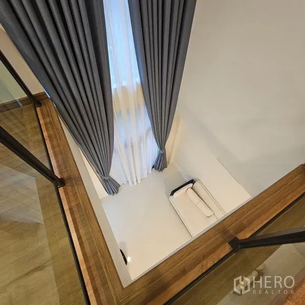 บ้าน ให้เช่าในSaphan Sung, Bangkok - มุมมองจากชั้นบนลงสู่โถงรับแขกเพดานสูง พร้อมผ้าม่านสูงจรดเพดานและโซฟา.