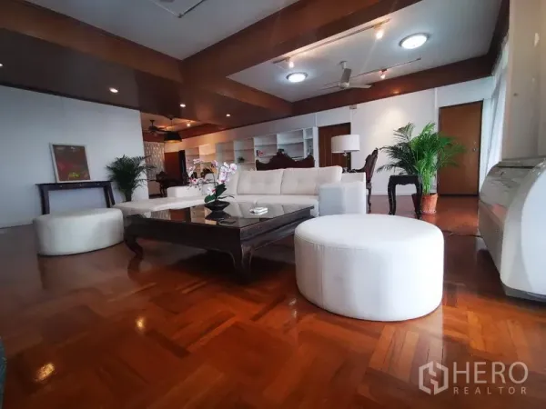 Apartment for rent in Khlong Toei, Bangkok - Spacious living room with parquet wood floors, white sofas, dark wood coffee table, ceiling fan and indoor plants.