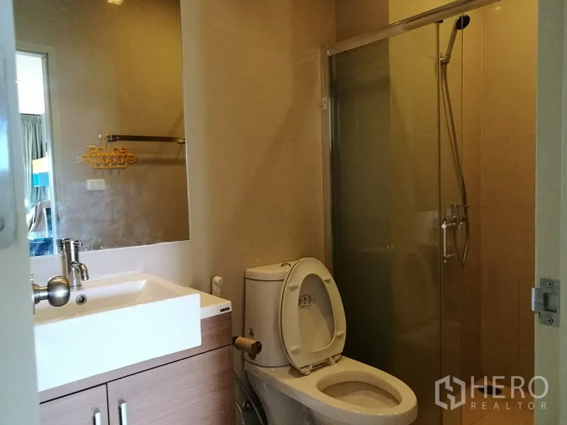 Condominium for rent in Watthana, Bangkok - Modern bathroom with glass-enclosed shower, toilet, large mirror and vanity sink.