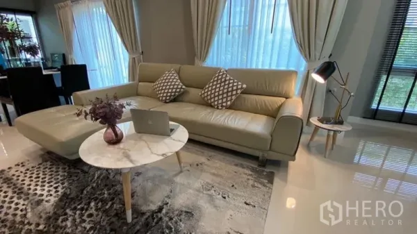 Detached House for rent in Samut Prakan - Living room with L-shaped leather sofa, marble coffee tables and floor lamp by large windows.