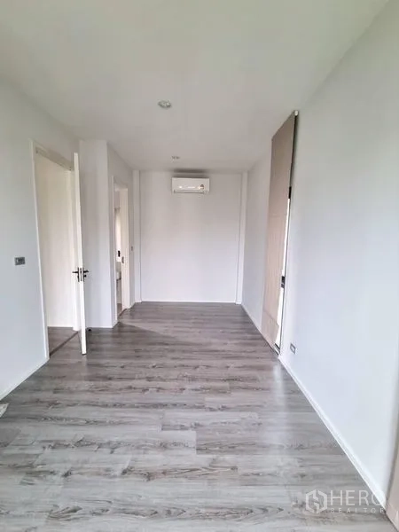 独立式住宅 出租 - 明亮的楼上房间，灰色木地板、白墙，带壁挂空调与门。