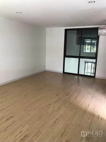 Townhouse for rent in Wang Thonglang, Bangkok - Upper-floor room with wood-look flooring, black-framed window, and air conditioner.