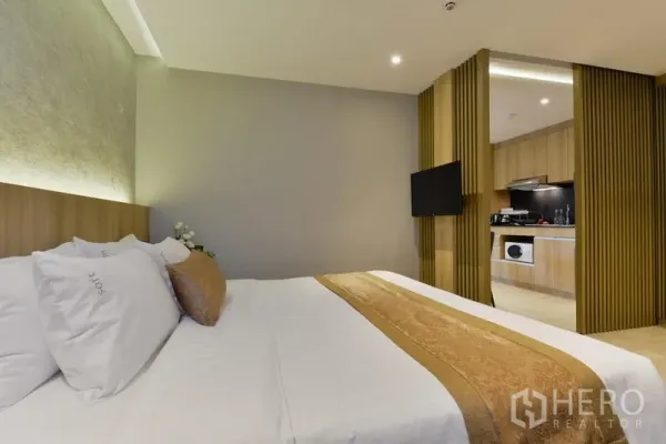 Apartment for rent in Khlong Toei, Bangkok - Bedroom suite with soft lighting and view into an open kitchen through a slatted divider.