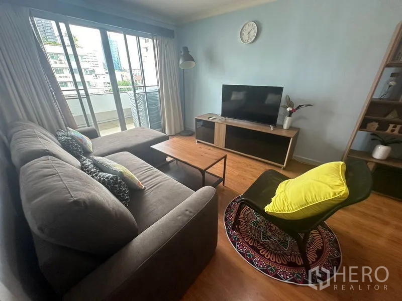 Condominium for rent in Watthana, Bangkok - Living area with sectional sofa, accent chair, TV and sliding doors to a small balcony.