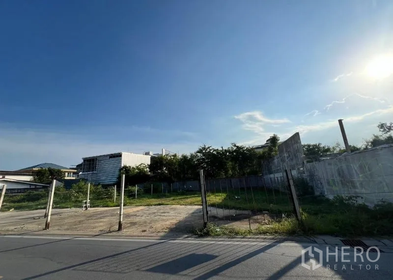 ที่ดิน ขายในBang Na, Bangkok - ที่ดินเปล่าติดถนนในบางนา มีกำแพงรอบบางส่วนและรั้วชั่วคราว ใต้ท้องฟ้าสดใส