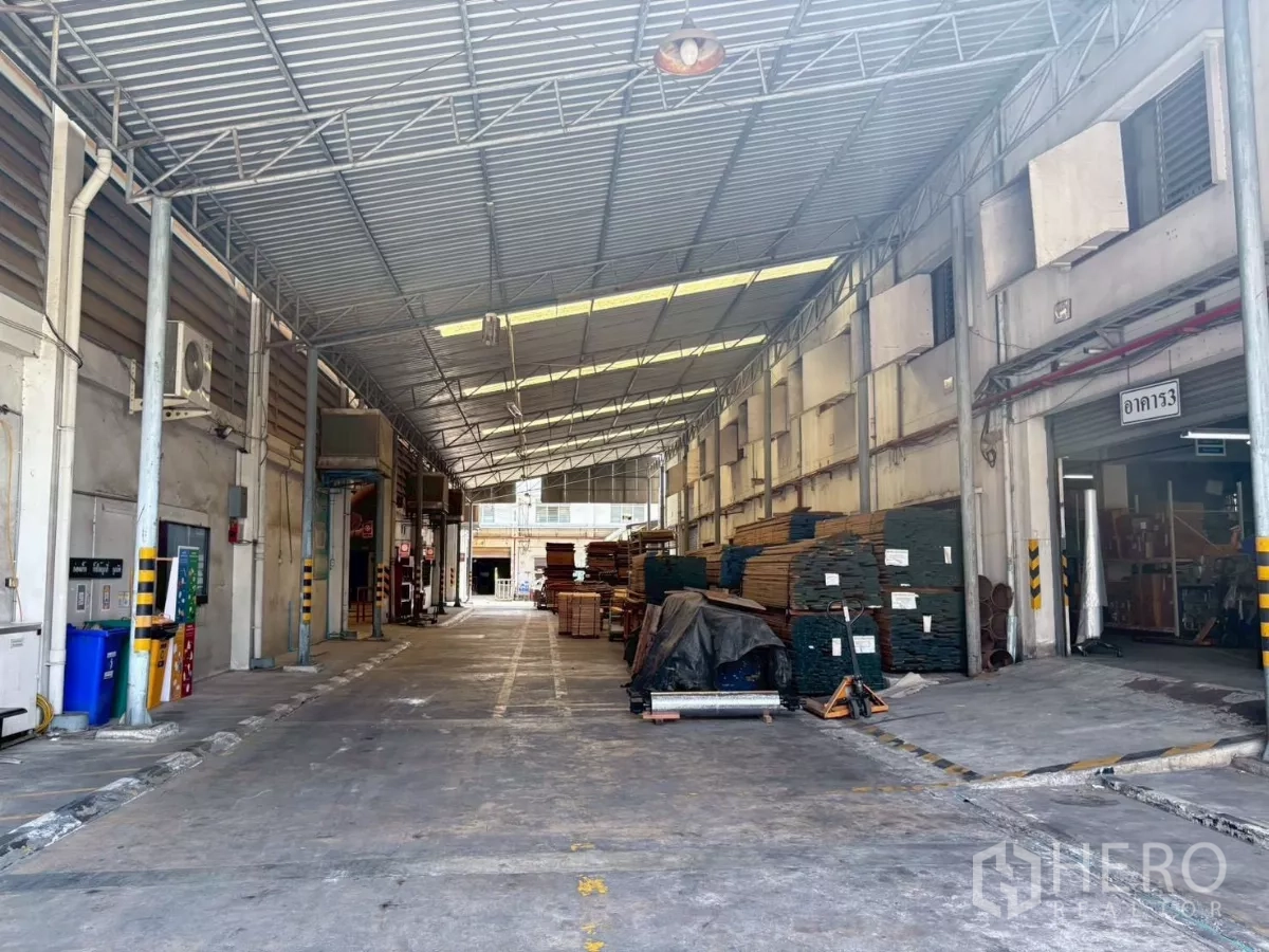 工厂 出租或出售在Bang Khun Thian, Bangkok - 建筑之间的有顶装卸通道，堆放材料与楼栋标识。