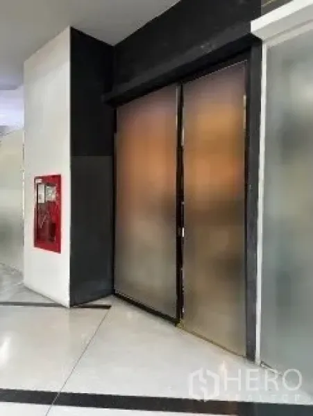 零售空间 出租在Khlong Toei, Bangkok - 走廊旁紧凑店面，磨砂玻璃门板，邻近红色消防设备柜。