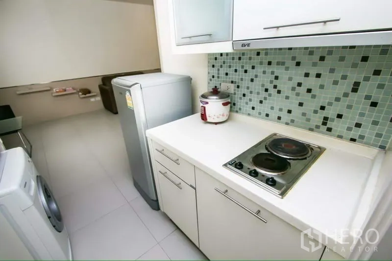 公寓 出租在Ratchathewi, Bangkok - 小厨房配电磁炉、冰箱、马赛克背墙与洗衣机，可见客厅。