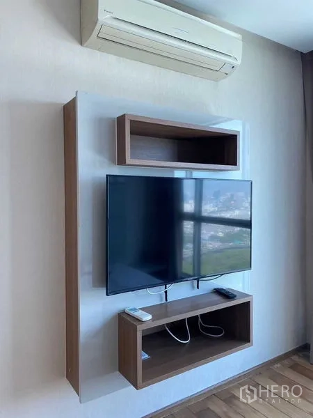 Condominium for sale in Ratchathewi, Bangkok - Wall-mounted TV unit with shelving under split-type air conditioner and city reflection on screen.