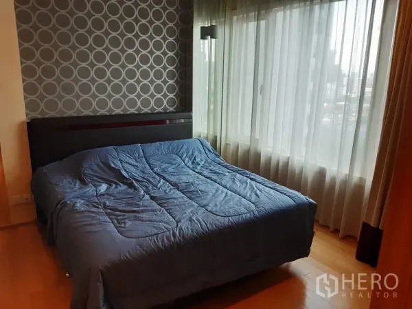 คอนโด ให้เช่าในKhlong Toei, Bangkok - ห้องนอนสว่างโปร่ง หน้าต่างบานใหญ่ วิวเมือง ผนังลายกราฟิก และเตียงควีนพร้อมผ้าคลุมสีน้ำเงิน