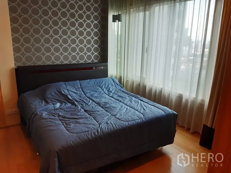 คอนโด ให้เช่าในKhlong Toei, Bangkok - ห้องนอนสว่างโปร่ง หน้าต่างบานใหญ่ วิวเมือง ผนังลายกราฟิก และเตียงควีนพร้อมผ้าคลุมสีน้ำเงิน