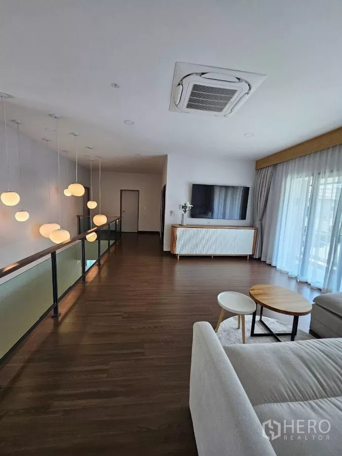 Detached House for rent or sale in Bang Phli, Samut Prakan - Upstairs family room with wood floors, sofa, TV console, balcony curtains, and ceiling cassette air‑conditioning.