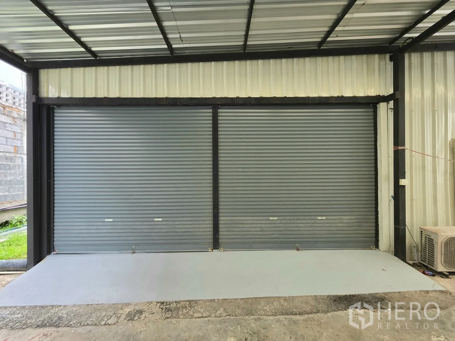 Warehouse for rent in Suan Luang, Bangkok - Front view of double roller shutters under a metal canopy.