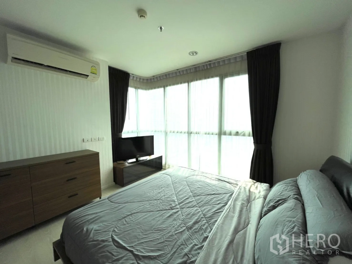Condominium for sale in Sathon, Bangkok - Master bedroom corner with wraparound windows, wood dresser and TV stand.