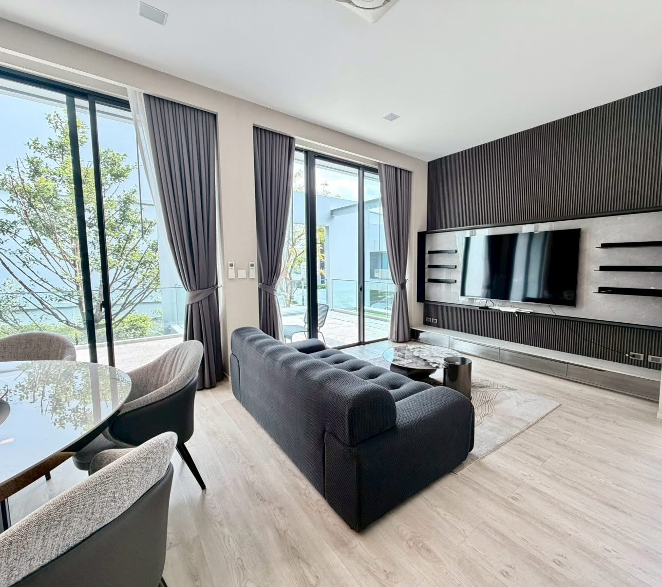 Detached House for rent in Saphan Sung, Bangkok - Sunny living room with sliding glass doors, curtains and a TV feature wall facing a plush sofa.