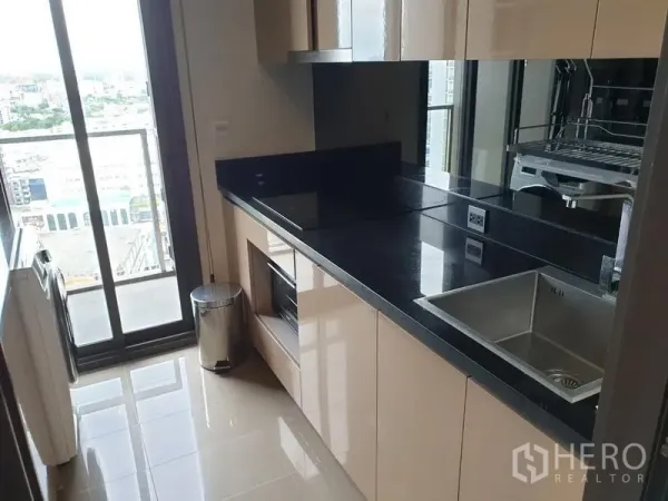 คอนโด ให้เช่าในWatthana, Bangkok - ครัวแบบแกลเลอรี ตู้ลามิเนตเงา เคาน์เตอร์หินสีดำ อ่างล้างจาน และประตูออกระเบียงวิวเมือง