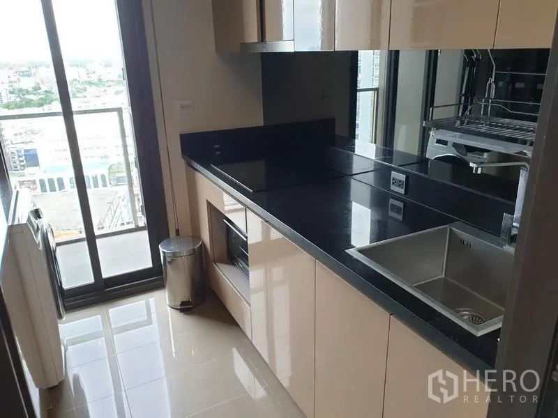 คอนโด ให้เช่าในWatthana, Bangkok - ครัวแบบแกลเลอรี ตู้ลามิเนตเงา เคาน์เตอร์หินสีดำ อ่างล้างจาน และประตูออกระเบียงวิวเมือง