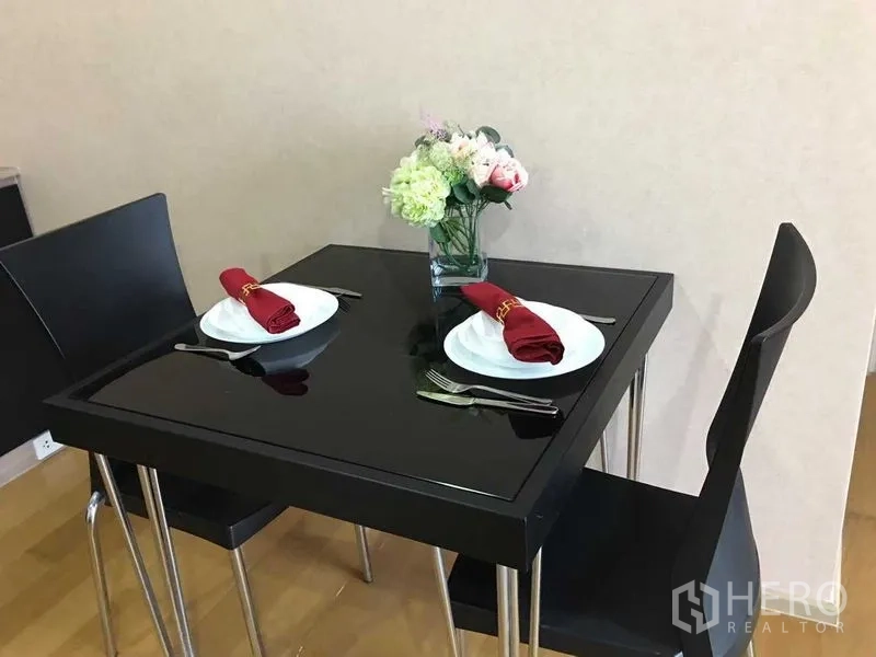 Condominium for sale in Khlong San, Bangkok - Compact black glass dining table set for two with red napkins on wood flooring.