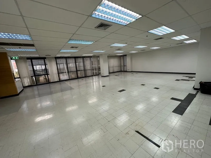 Office Space for rent in Khlong Toei, Bangkok - Large work area with ceiling lights, pillars and vertical blinds along the glass facade.