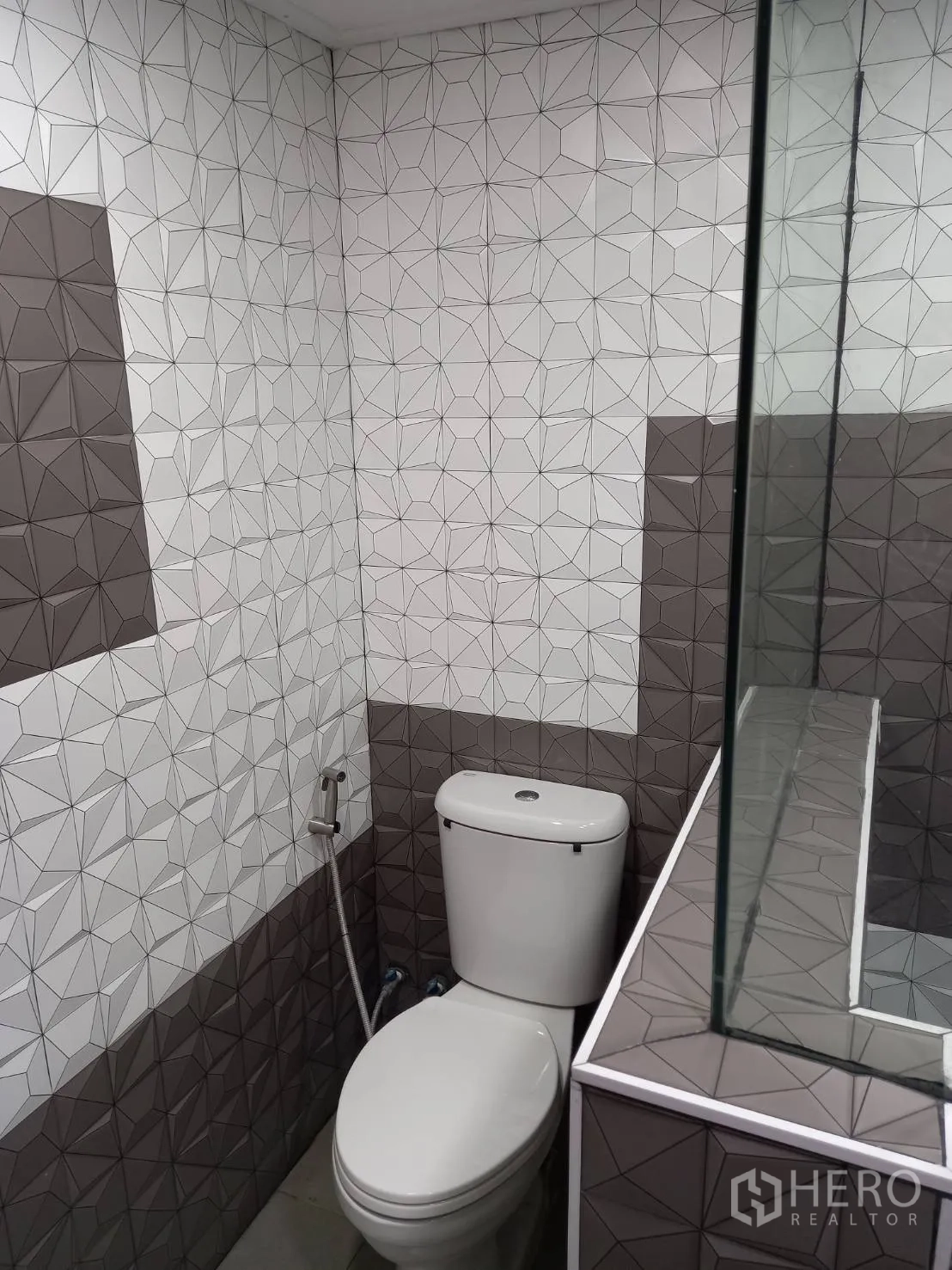 公寓 出租在Khlong Toei, Bangkok - 坐便区带喷枪，几何图案墙砖，旁为淋浴玻璃隔断。