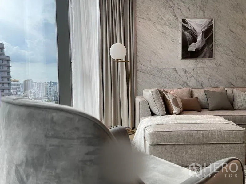 公寓 出租在Watthana, Bangkok - 客厅配L形沙发与大理石背景墙，窗帘高挑框出城市景观。