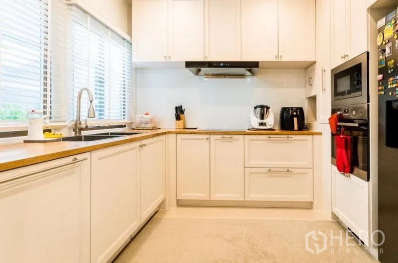 独立式住宅 出租 - U形厨房，白色橱柜、木质台面，窗边水槽与嵌入电器。