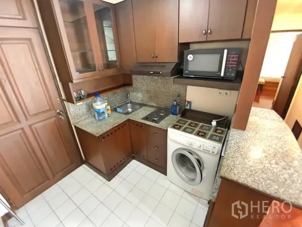 公寓 出租在Bang Rak, Bangkok - U 形厨房，木质橱柜、花岗岩台面、灶台、微波炉、抽油烟机及室内洗衣机。