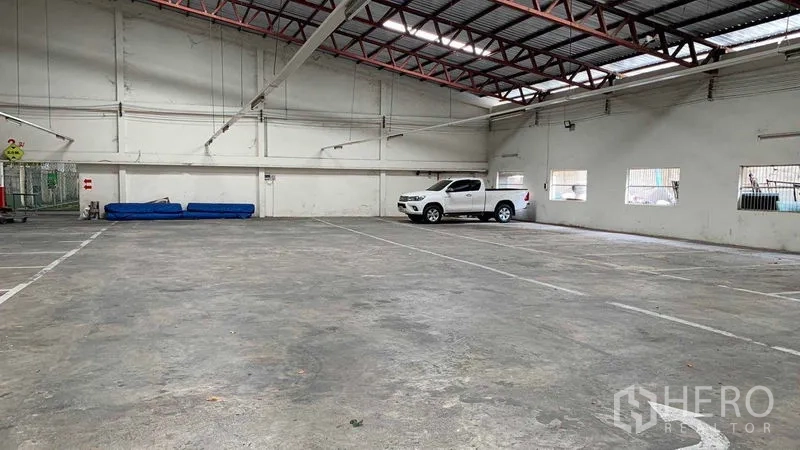 Warehouse for rent in Phra Pradaeng, Samut Prakan - Empty warehouse bay with metal truss roof and marked parking lines.
