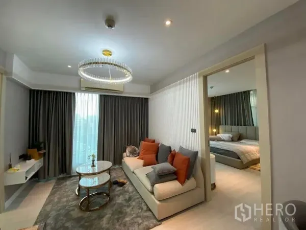 Condominium for sale in Huai Khwang, Bangkok - Living room with crystal-ring chandelier, sliding door to bedroom and floor-to-ceiling curtained window.