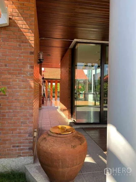 Detached House for rent in Bang Phli, Samut Prakan - Covered walkway with terracotta tiles, sliding glass doors and a decorative clay jar beside brick walls.