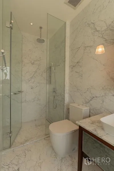 公寓 出租在Watthana, Bangkok - 大理石浴室，玻璃雨淋淋浴间、现代坐便器与台上盆。