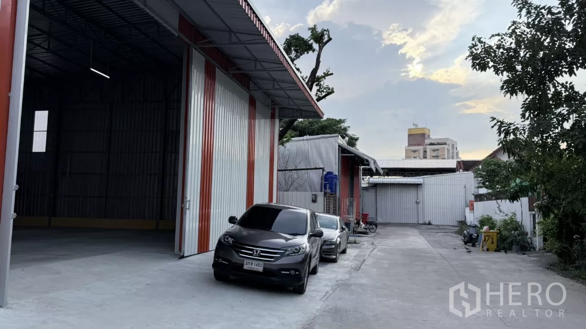 Warehouse for rent in Wang Thonglang, Bangkok - Driveway beside the warehouse with open bay and multiple parking spaces in a quiet compound.