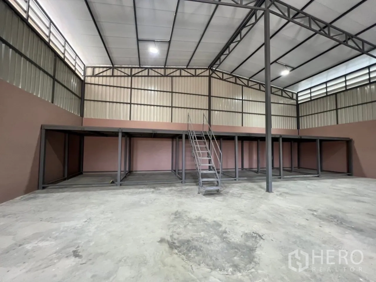 Warehouse for rent in Bang Bua Thong, Nonthaburi - Spacious warehouse interior showing high ceiling, steel trusses and mezzanine with stairs.