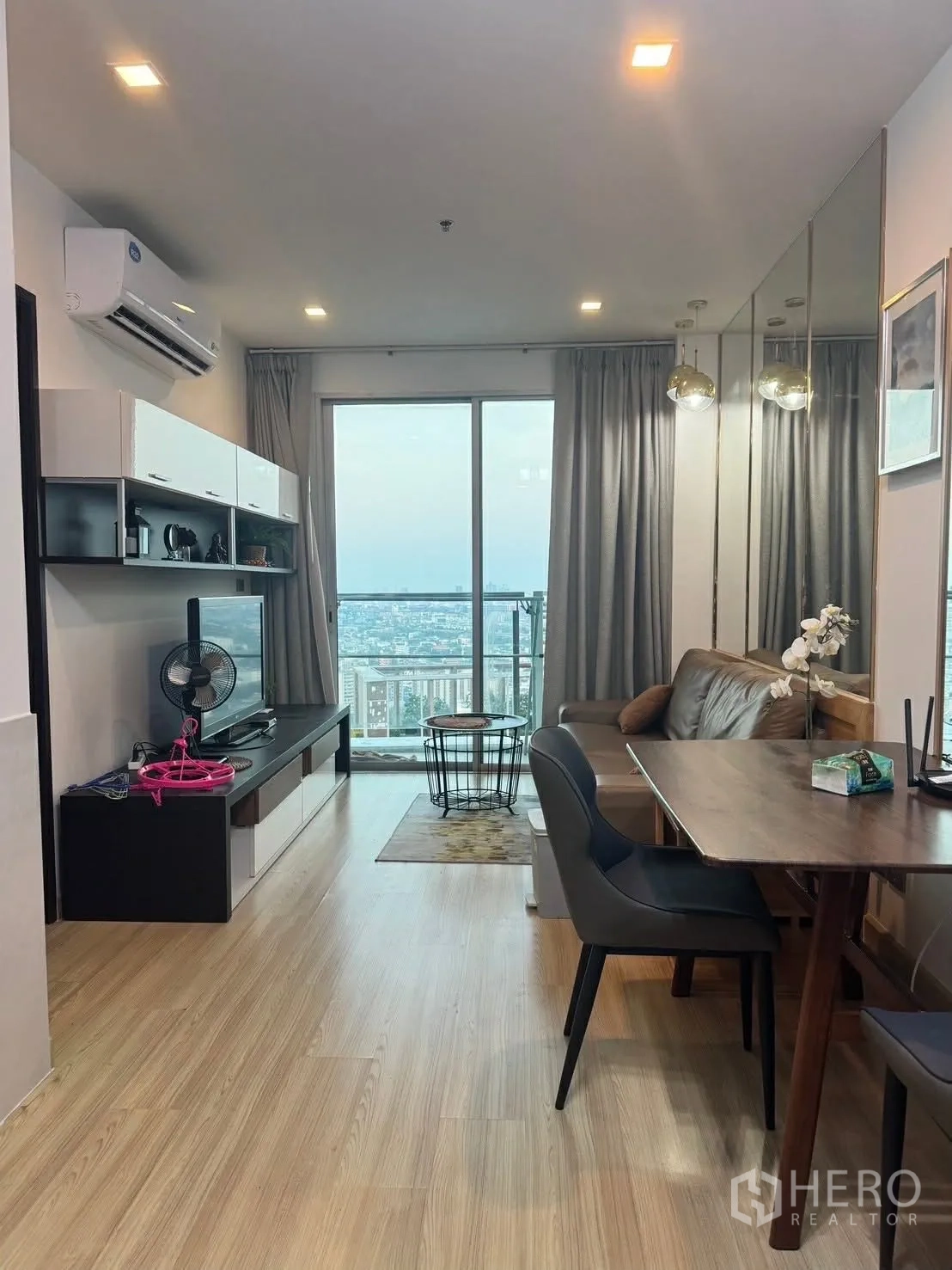 Condominium for rent in Watthana, Bangkok - Open-plan living and dining area with TV console, leather sofa, and balcony doors overlooking the city.