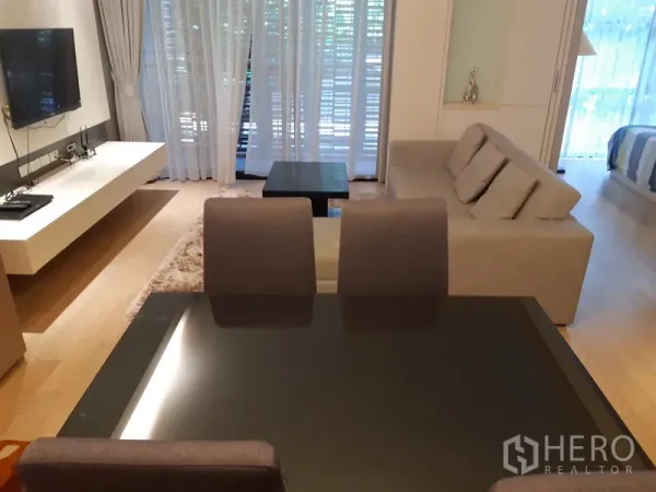 คอนโด ให้เช่าในWatthana, Bangkok - โต๊ะอาหาร 4 ที่นั่งหันหน้าไปยังห้องนั่งเล่น มีทีวีติดผนัง ผ้าม่านโปร่งและวิวต้นไม้ที่ระเบียง