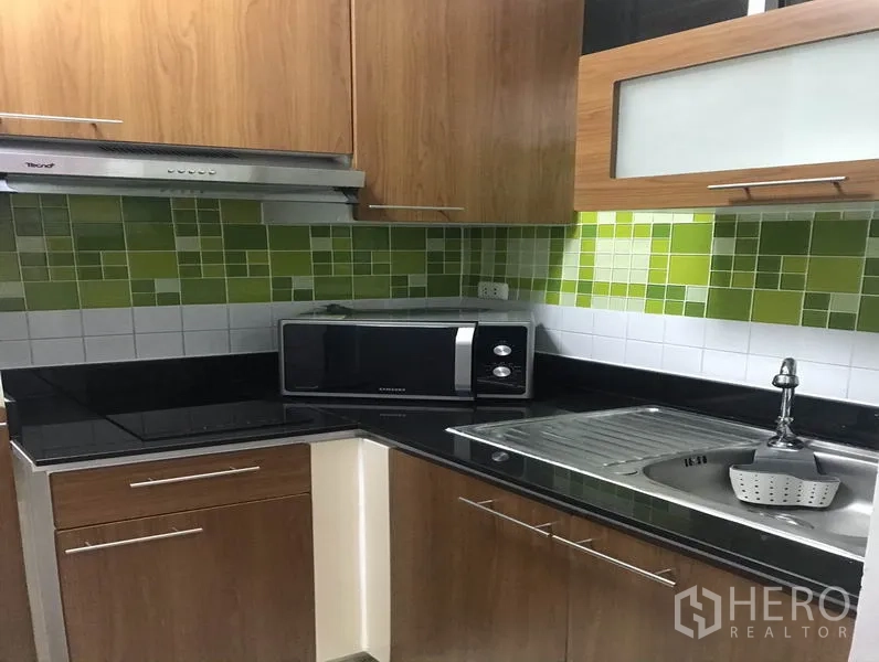 คอนโด ให้เช่าหรือขายในKhlong Toei, Bangkok - ครัวรูปตัวแอล เคาน์เตอร์สีดำ ตู้ไม้ กระเบื้องโมเสคสีเขียว ไมโครเวฟ และซิงก์