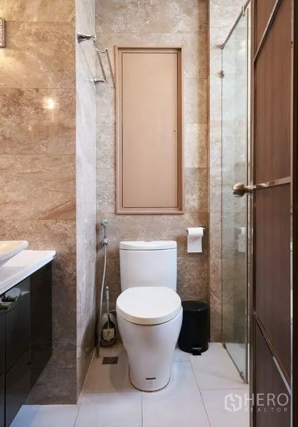 Condominium for sale in Ratchathewi, Bangkok - Marble-tiled bathroom with glass shower, modern toilet and vanity in a Bangkok condo.