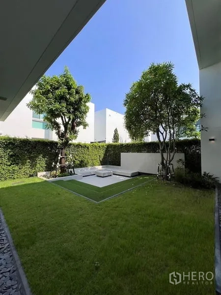 Detached House for sale in Samut Prakan - Private landscaped garden with lawn, mature trees, and tall hedge fence.